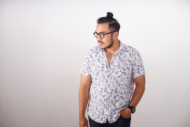 man with man bun poses against wall