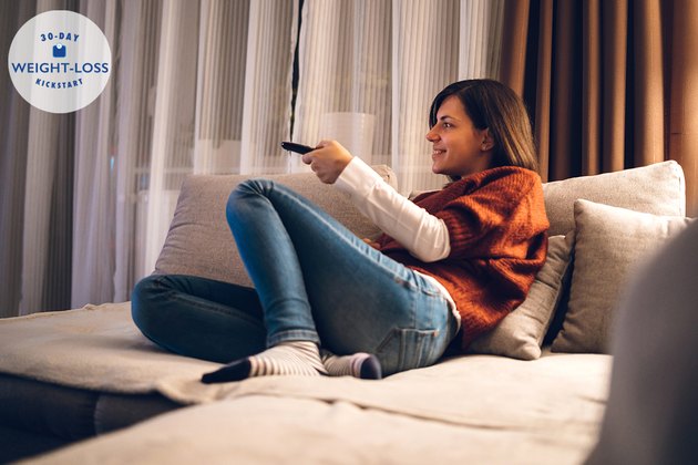 A woman doing intermittent fasting sitting on the couch watching TV at night