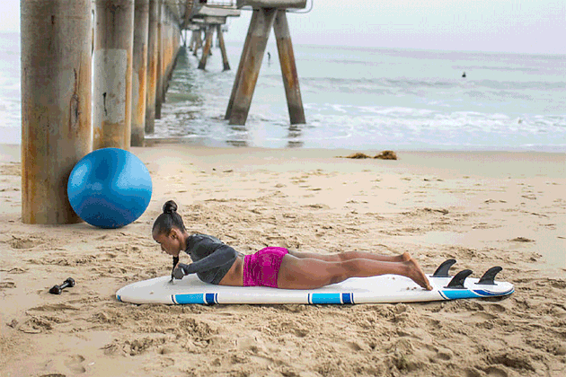woman doing Shoulder Clock exercise on surfboard on the beach