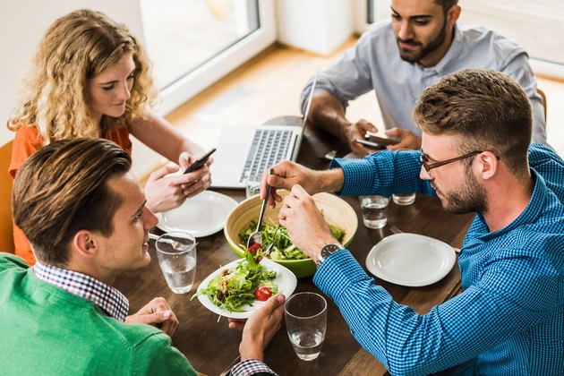 Women and men having a working lunch, man serving salad