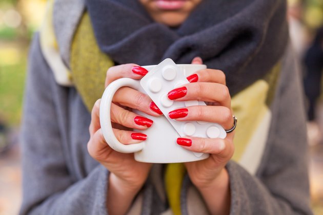 Ill sad girl with hot drink and medicine in the park. Autumn tim