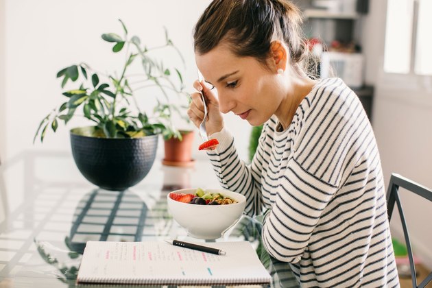 Woman eating breakfast and reading food journal