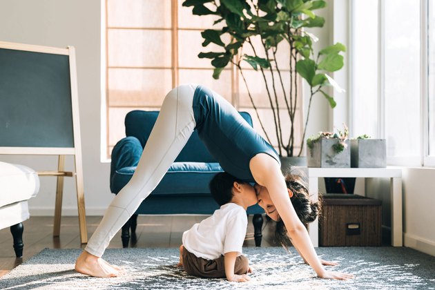 Woman doing downward dog yoga pose with her son in living room