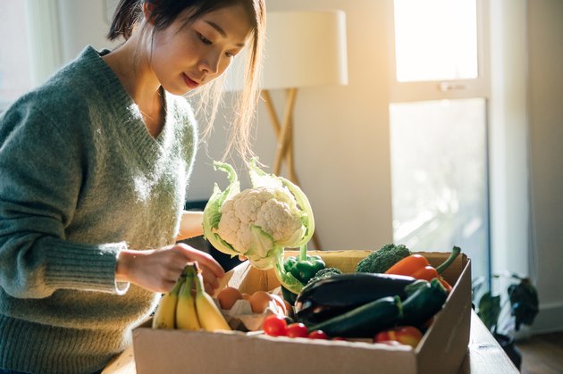 woman unpacking cardboard box of groceries holding cabbage