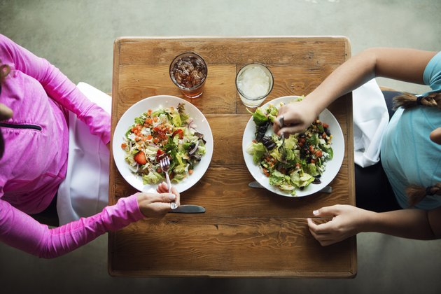 Overhead shot of two women eating salads at a restaurant practicing portion control