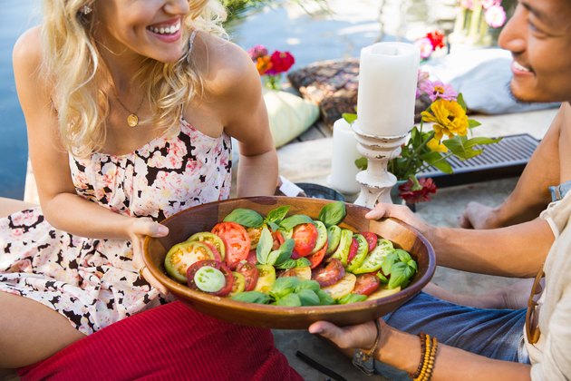 Man and woman passing a tomato salad at a summer picnic