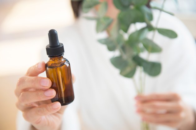 Woman holding a eucalyptus plant and a bottle of essential oils