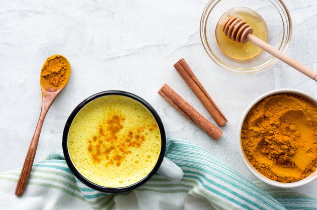 Turmeric latte, cooking golden milk with honey and cinnamon. Concrete background. Top≠