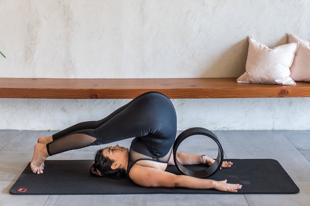 woman doing Plow Pose (Halasana) with a yoga wheel