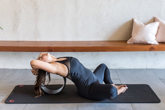 woman doing Reclined Easy Sitting Pose (Supta Sukhasana) with a yoga wheel