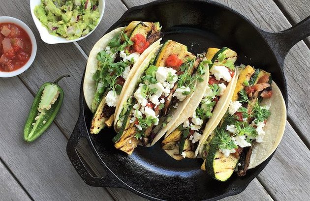 A cast-iron pan with four grilled veggie tacos, and a side of guacamole and salsa