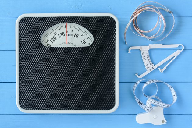Mechanical weight scale, body mass control concept : Bathroom scale, personal accurate body fat tester / skin fold caliper measurement tool for stomach / belly and measuring tape on blue background