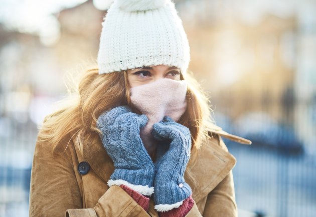A woman wearing a hat, scarf and gloves outside in the winter to prevent getting sick