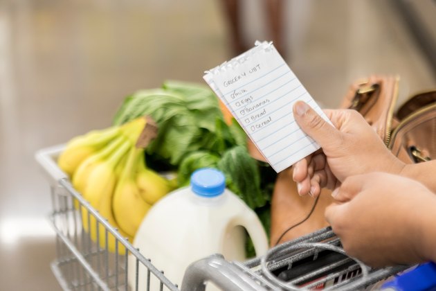 close up of woman's hands holding grocery list and cart with milk and bananas