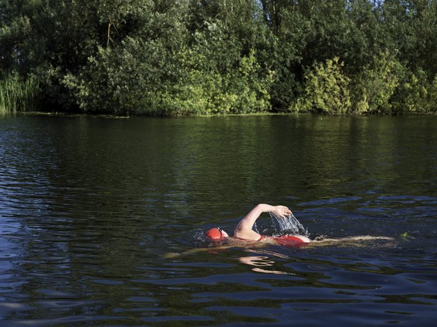 女子游自由式游泳在一条被树环绕的河里游