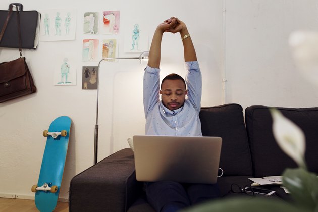 Overwhelmed businessman stretching hands while working on laptop in creative office