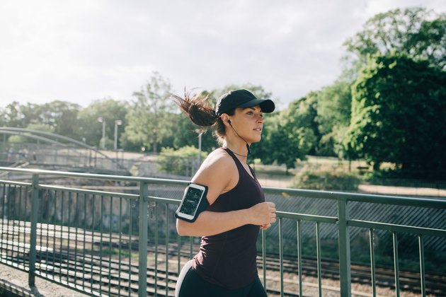自信的女运动员戴着耳机听着音乐在城市的桥上慢跑