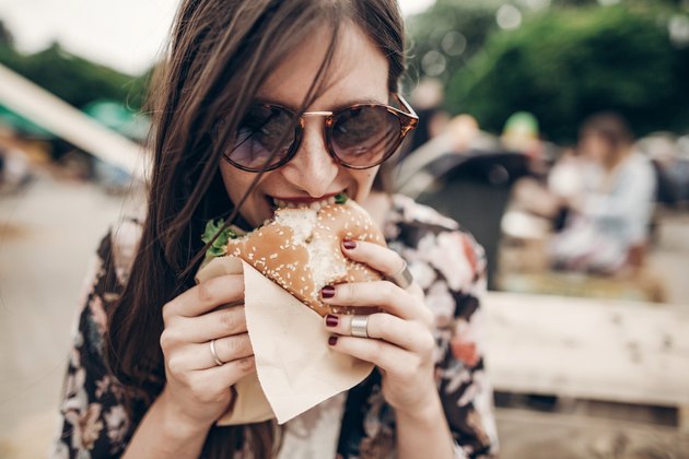 A stylish hipster woman eating a large turkey burger outside