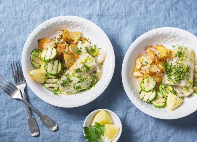Pan roasted pollock with fried potatoes and grilled zucchini on a blue background, top view. Delicious lunch