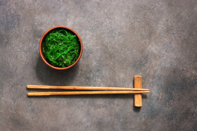 Wakame Chuka or seaweed salad with sesame seeds in bowl on dark brown rustic background. Traditional Japanese food. Top view, flat lay,copy space.