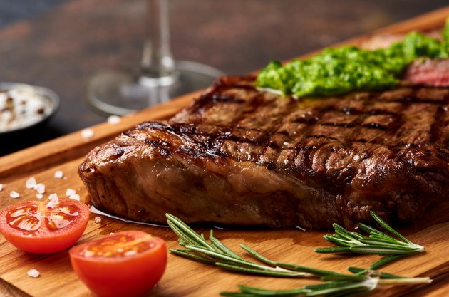 Grilled Black Angus Steak with tomatoes, garlic with chimichurri sauce on meat cutting board.