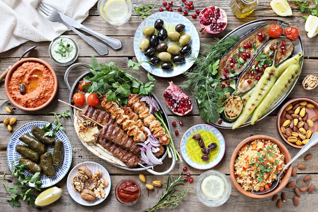 Middle eastern, arabic or mediterranean dinner table with grilled lamb kebab, chicken skewers with roasted vegetables and appetizers variety serving on rustic outdoor table.