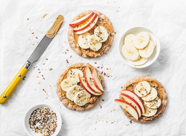 Peanut butter, apple, banana, flax and chia seed crackers toast on a light background, top view