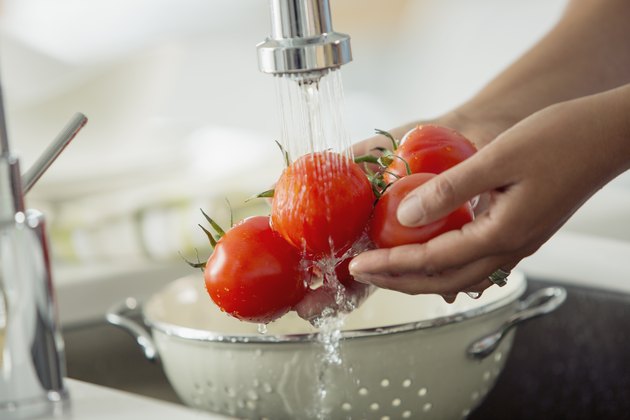 Woman rinsing tomatoes in sink with colander.