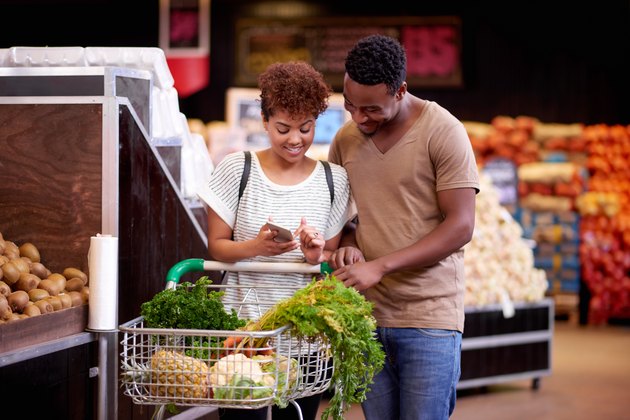 Man and woman in grocery store looking at phone ensuring they stay on track with their shopping budget