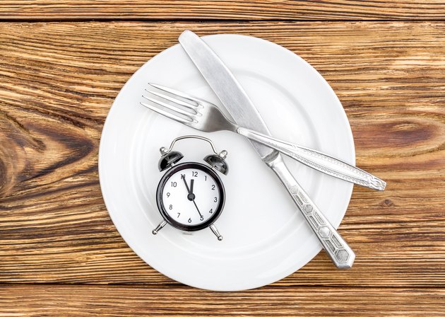Alarm clock with fork, knife and plate on the table. Top view. Time to eat.