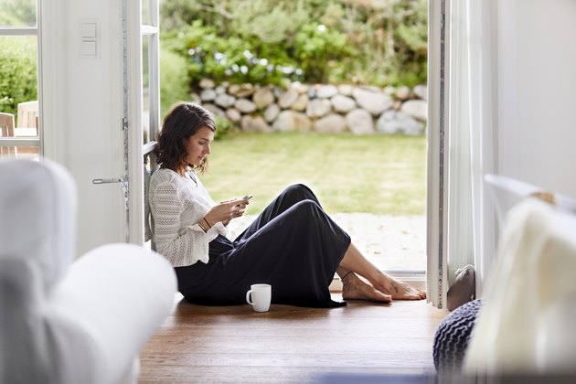Young woman sitting in windowframe using cell phone