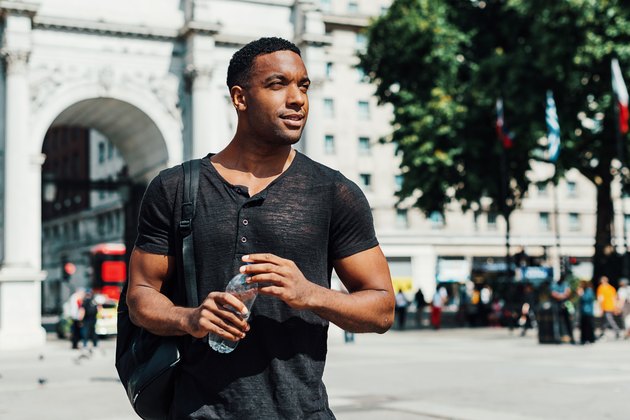 Afro-Caribbean guy in London with bottle of water practicing how to how to eat healthy on vacation