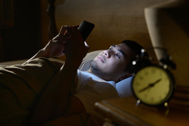 Young man with insomnia using a smartphone in his bed late at night