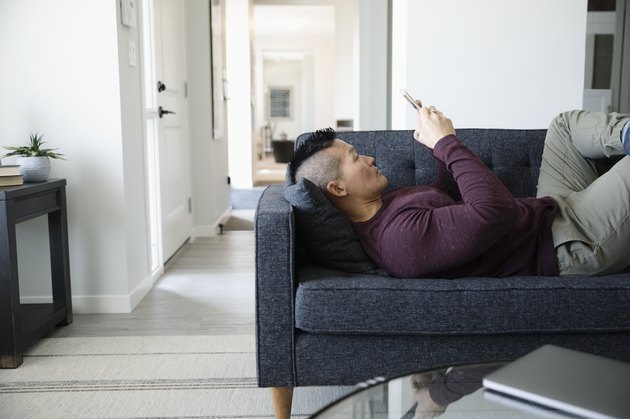 Man relaxing, using smart phone on living room sofa