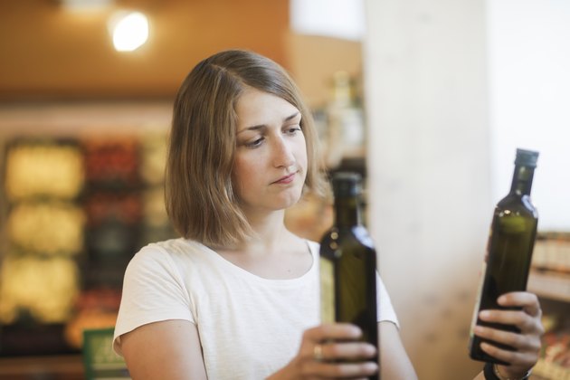 女子站在比较橄榄油瓶超市“itemprop=