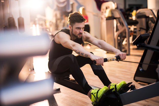 Determined man exercising on rowing machine in a gym.