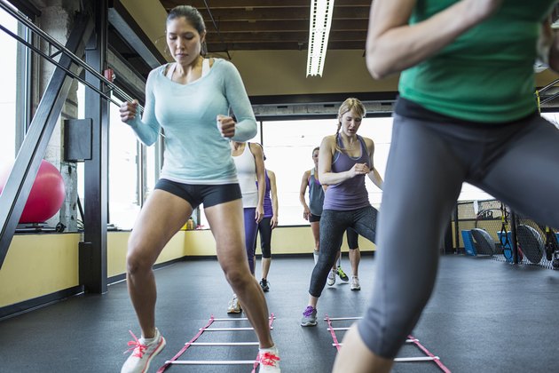 Instructor with women jumping over agility ladder in gym