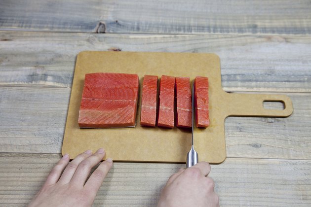 Chef chopping a fresh raw red salmon fillet with kitchen sharp knife