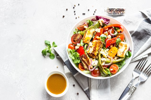 Vegetable salad cherry tomatoes, baked pepper, salad mix and onion with grilled haloumi (halloumi) cheese. Keto diet, healthy food. Light grey stone background.
