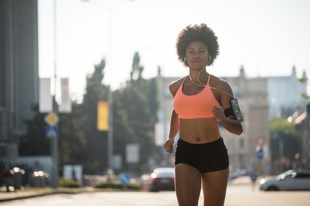 Athletic fitness girl running outdoors, enjoying music.