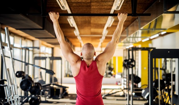 Close up back view of motivated and focused strong muscular active healthy young bald man working pull ups in the modern gym.