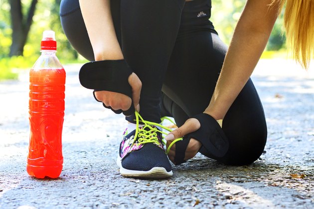 A female athlete tying her shoe with a sports drink next to her