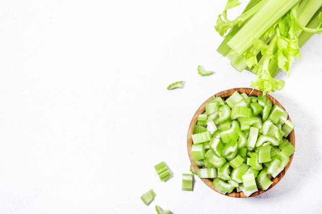 Fresh green celery chopped pieces in bowl, white background, top view, copy space