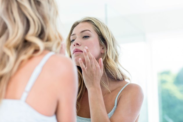 Focused beautiful young woman looking at herself in the bathroom mirror