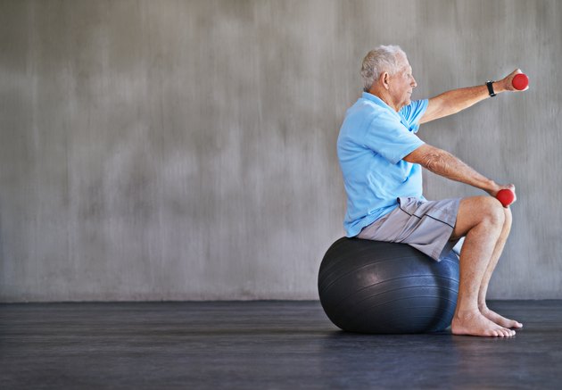 older man on stability ball doing reps and sets of dumbbell front raises