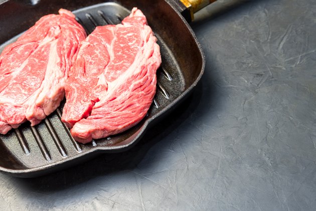 A raw marbled beef steak sits in a frying pan.