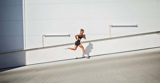 Young sportswoman running outdoors against wall