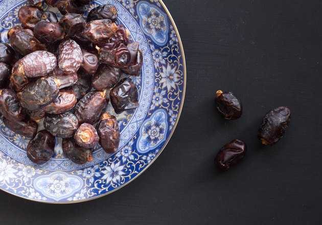 Top view of organic ready to eat dates in ornate blue and gold middle eastern plate on rustic black background with space for text