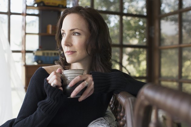 Pensive mature brunette woman drinking coffee at home