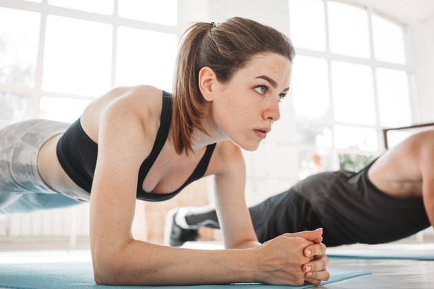 Young fit woman and man doing plank workout to improve her abs. Group people training cross work together